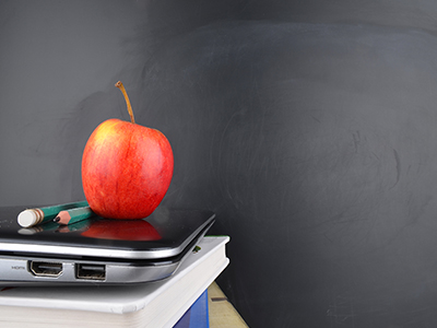 Pile of apple, pencils, laptop and book against black chalkboard