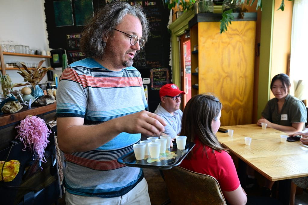 person bringing a tray of kombucha drinks to table