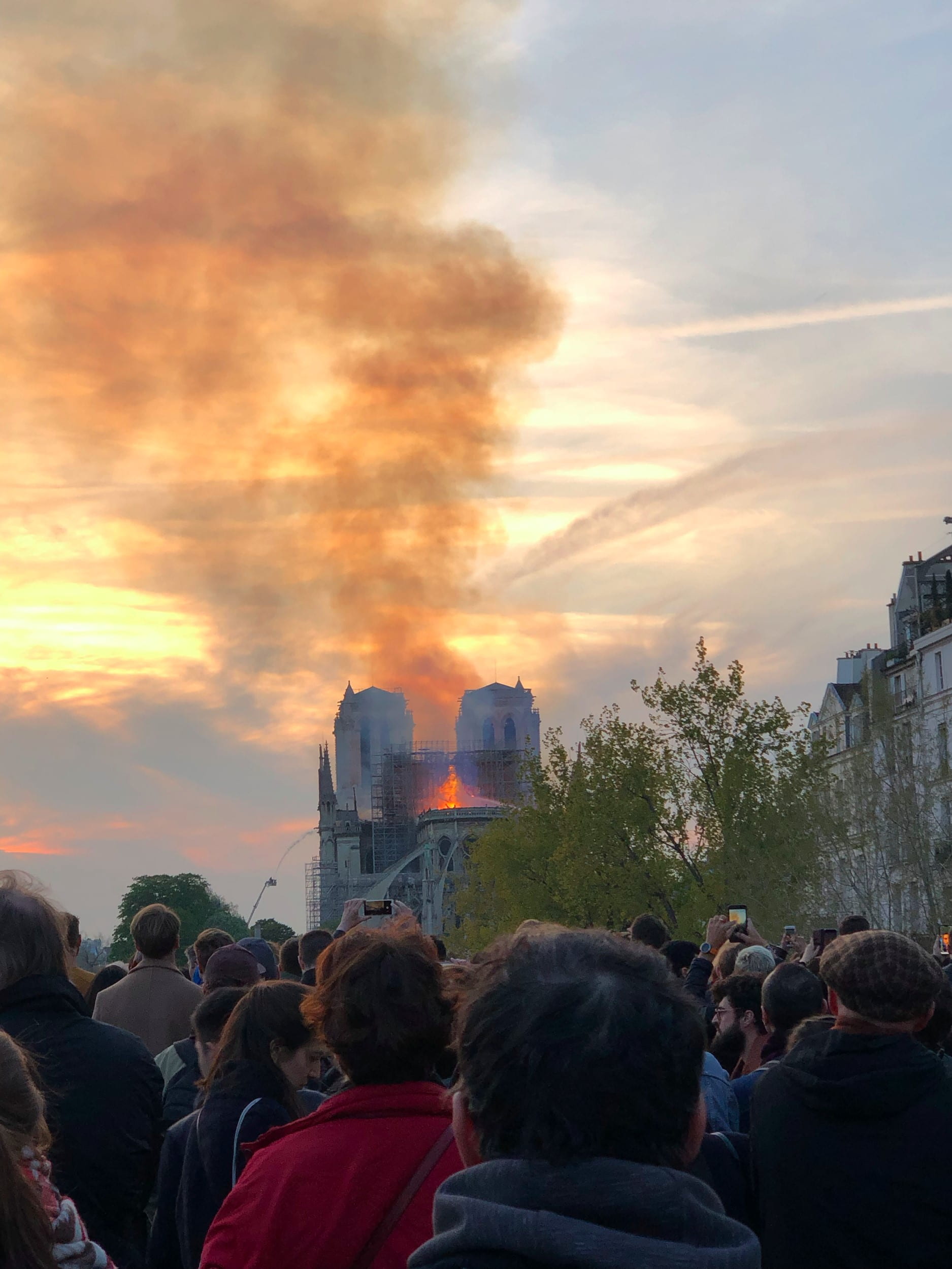 Lots of people watching the Notre Dame in Paris burn, flames and lots of smoke in the background